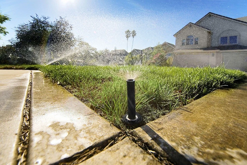 Irrigation sprinkler watering a front yard during spring start-up to keep the system flowing safely post-winter.