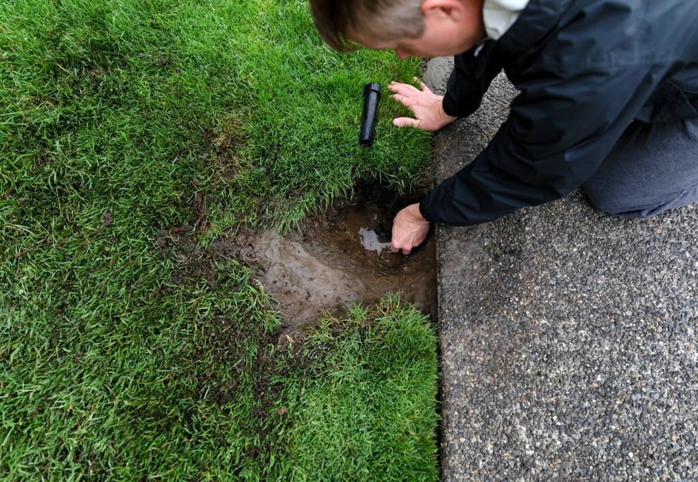 Technician checking lawn irrigation system for damage to avoid pipe bursts after winter shutoff.