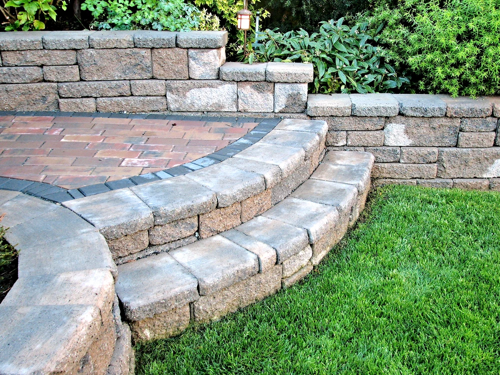 Retaining walls with textured block design supporting a raised planting bed with drought-tolerant landscaping.